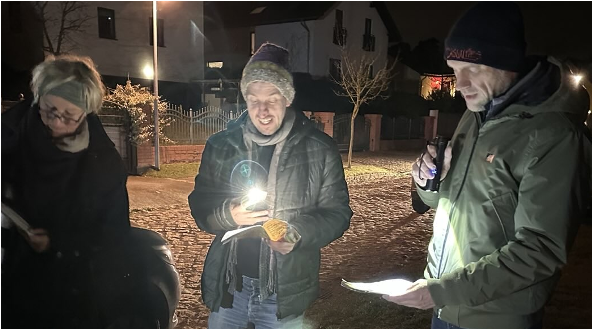 drei Menschen singen, es ist Abend, schauen auf Liedtexte mit Taschenlampen