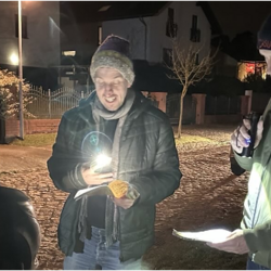 drei Menschen singen, es ist Abend, schauen auf Liedtexte mit Taschenlampen