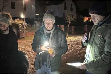 drei Menschen singen, es ist Abend, schauen auf Liedtexte mit Taschenlampen