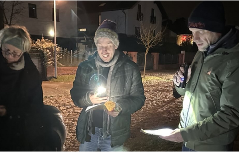 drei Menschen singen, es ist Abend, schauen auf Liedtexte mit Taschenlampen