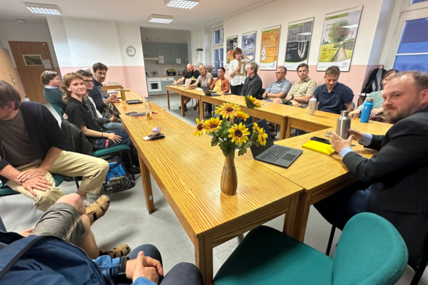 Mitglieder der BÜNDNIS 90 / DIE GRÜNEN sitzen um einen Tisch, rechts in der Ecke ist Clemens Rostock, Landesvorstand Brandenburg, zu sehen, auf dem Tisch steht eine Vase mit Sonnenblumen dem Logo der Grünen