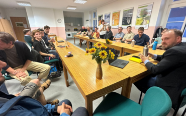 Mitglieder der BÜNDNIS 90 / DIE GRÜNEN sitzen um einen Tisch, rechts in der Ecke ist Clemens Rostock, Landesvorstand Brandenburg, zu sehen, auf dem Tisch steht eine Vase mit Sonnenblumen dem Logo der Grünen