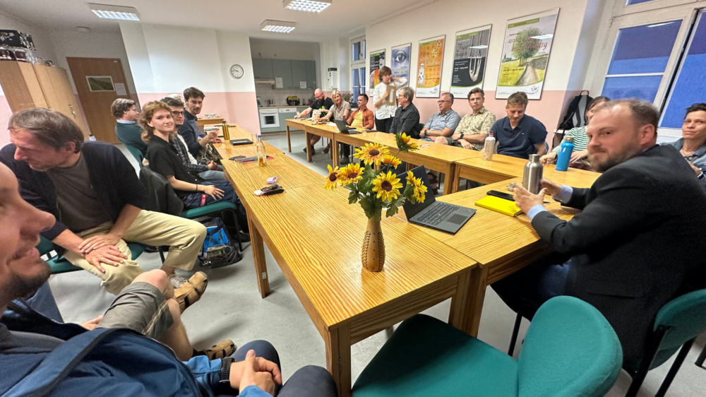 Mitglieder der BÜNDNIS 90 / DIE GRÜNEN sitzen um einen Tisch, rechts in der Ecke ist Clemens Rostock, Landesvorstand Brandenburg, zu sehen, auf dem Tisch steht eine Vase mit Sonnenblumen dem Logo der Grünen