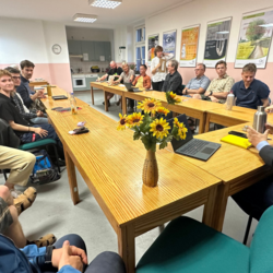 Mitglieder der BÜNDNIS 90 / DIE GRÜNEN sitzen um einen Tisch, rechts in der Ecke ist Clemens Rostock, Landesvorstand Brandenburg, zu sehen, auf dem Tisch steht eine Vase mit Sonnenblumen dem Logo der Grünen